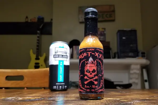 Bottl of Projet XXX Wing Hot Sauce with a 1000 Islands Brewery Beer in the background