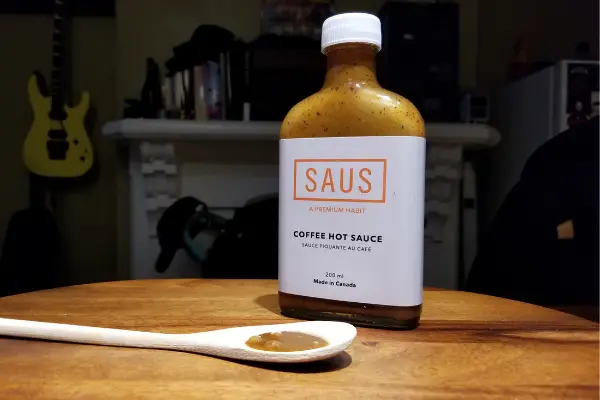 A spoon with some hot sauce and a bottle of Coffee Hot Sauce by Saus